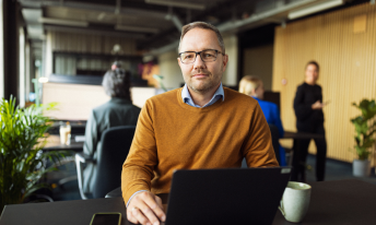 En mand sidder ved sin computer og kigger i kameraet