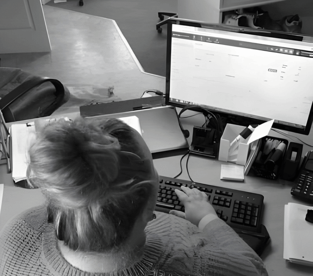 Billedet er taget oppefra og forestiller en kvinde bagfra, der sidder ved en computer