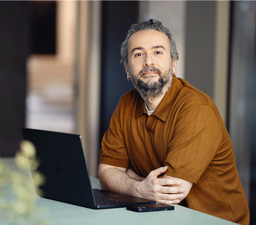 Et billede af en mand, der står ved en computer og kigger ind i kameraet