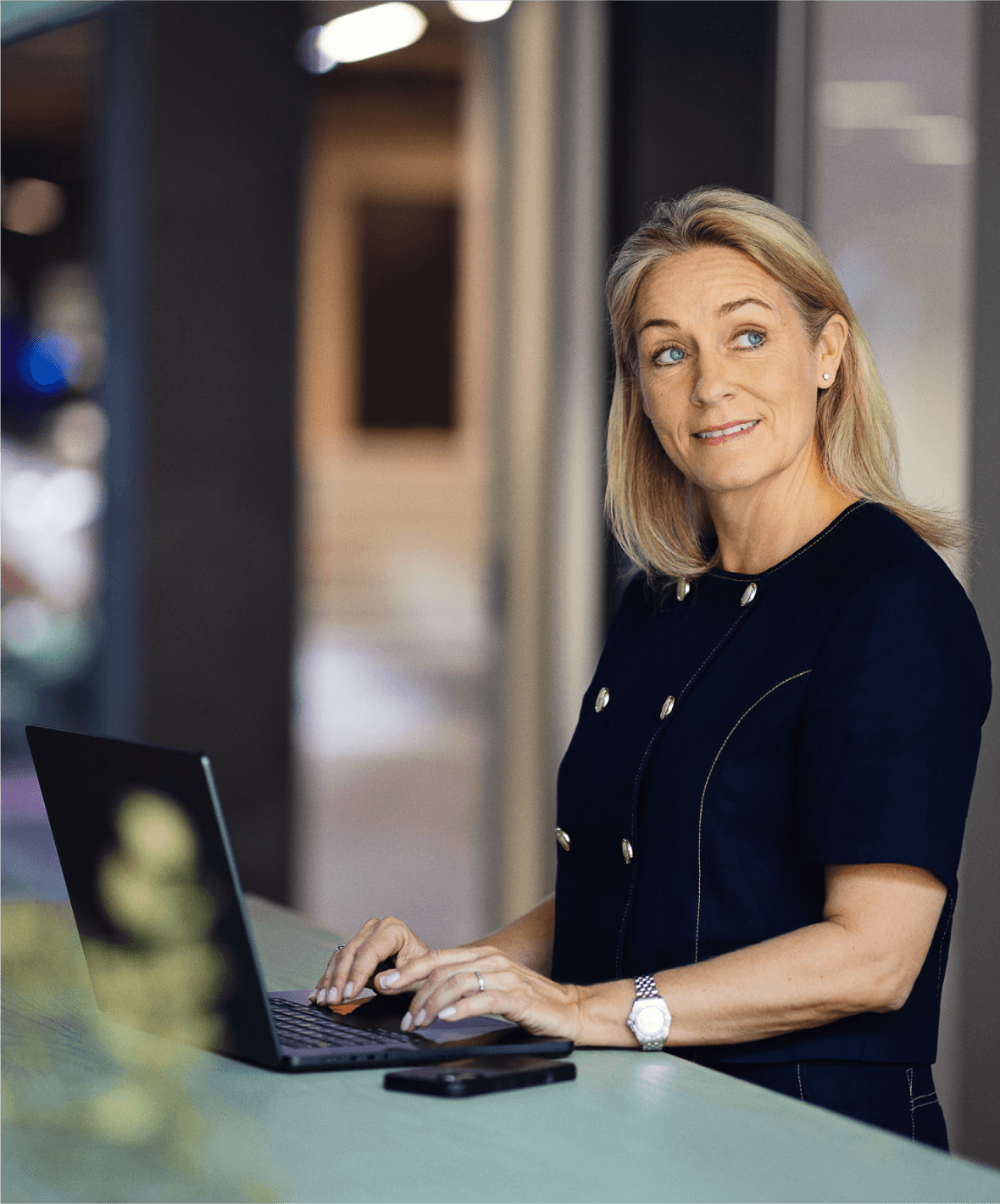 Et billede af en kvinde, der står og taster på en computer, mens hun kigger ud i luften