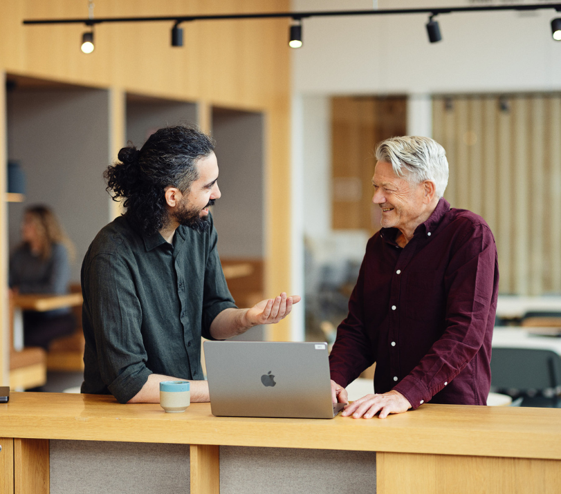 To mænd står og snakker sammen foran en computer