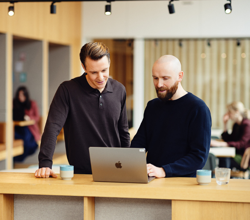 To mænd står og snakker sammen foran en computer