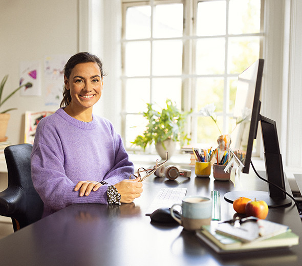 En kvinde sidder ved sit skrivebord og smiler