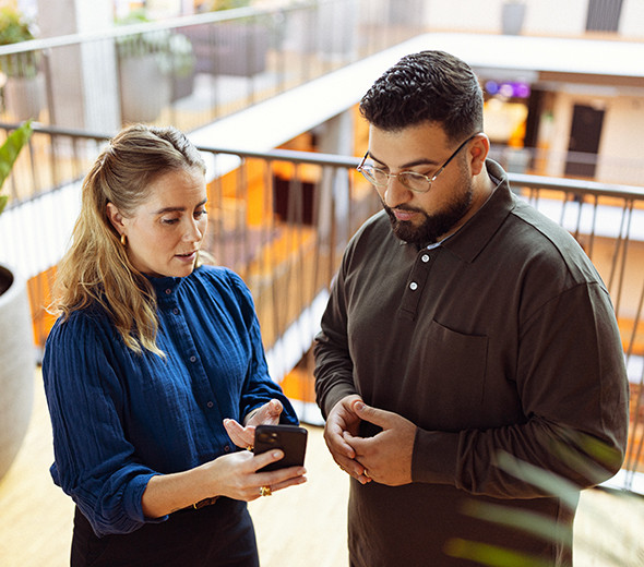 To personer står på en arbejdsplads og kigger på en telefon