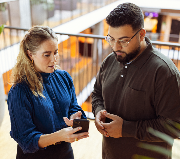 To personer står og kigger ned på en telefon