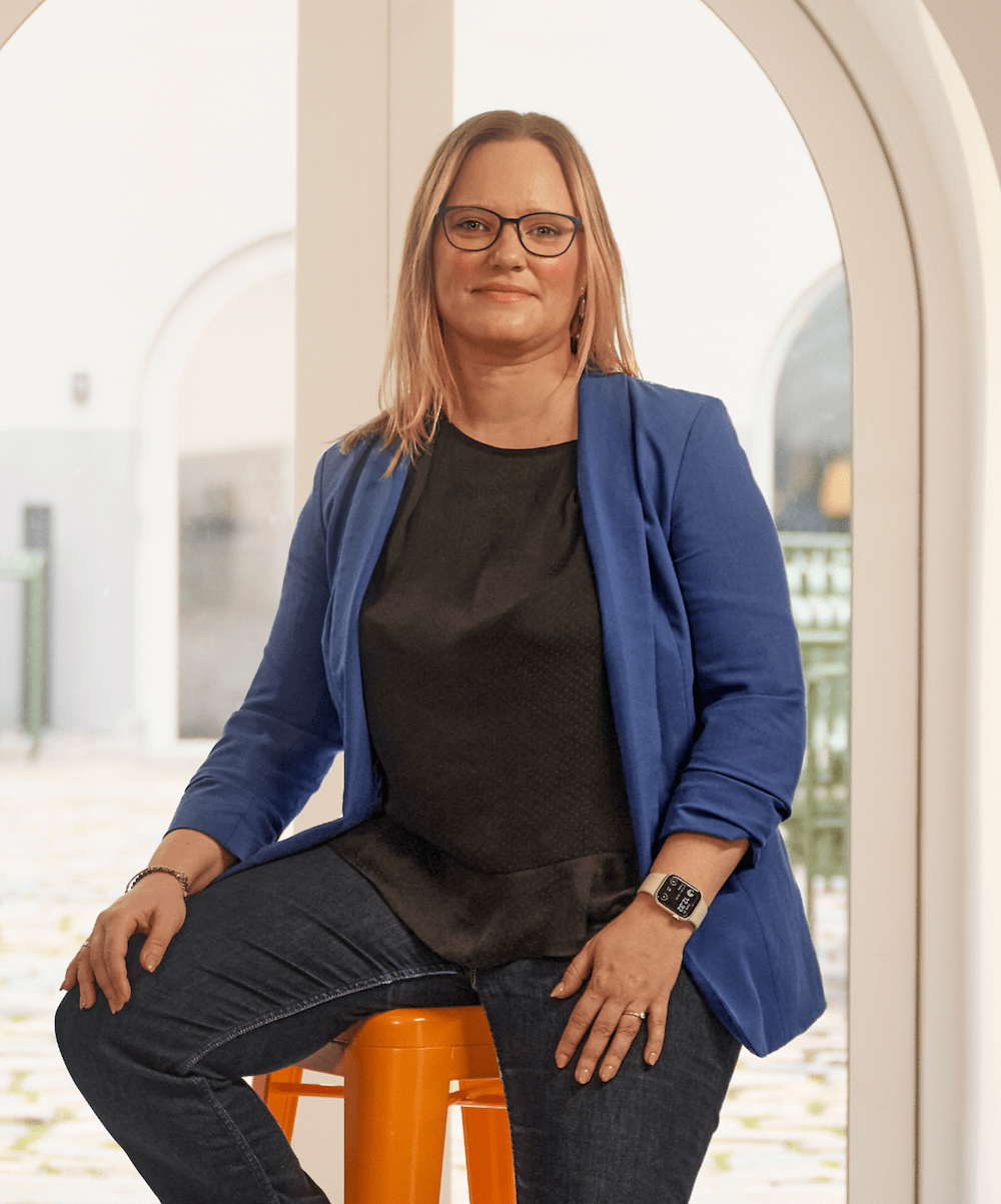 En kvinde sider på en orange tabutet foran et stort vindue