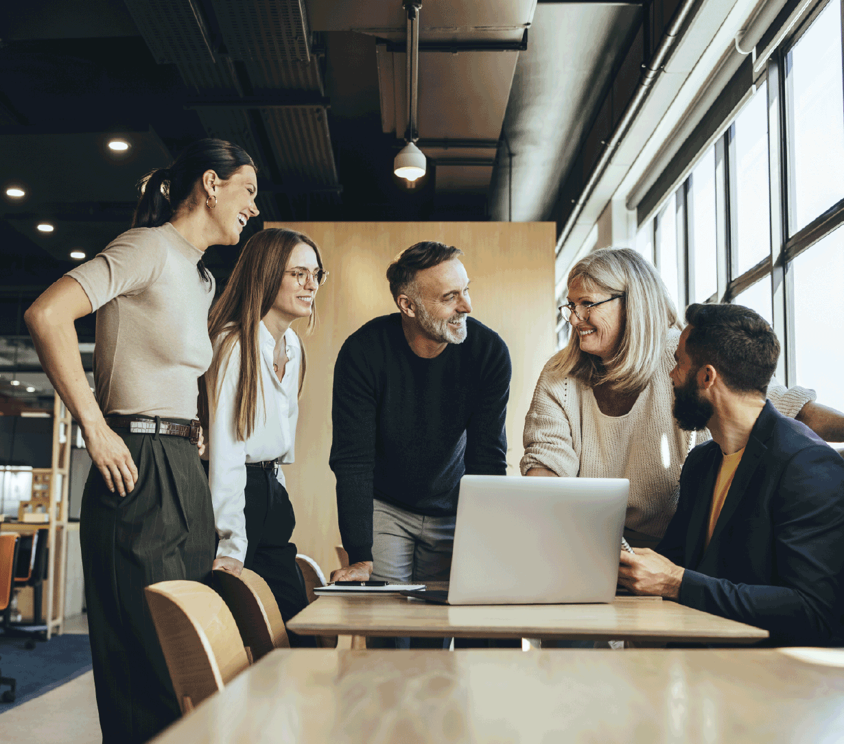 Fem mennesker står rundt om et skrivebord og snakker sammen, mens de alle smiler