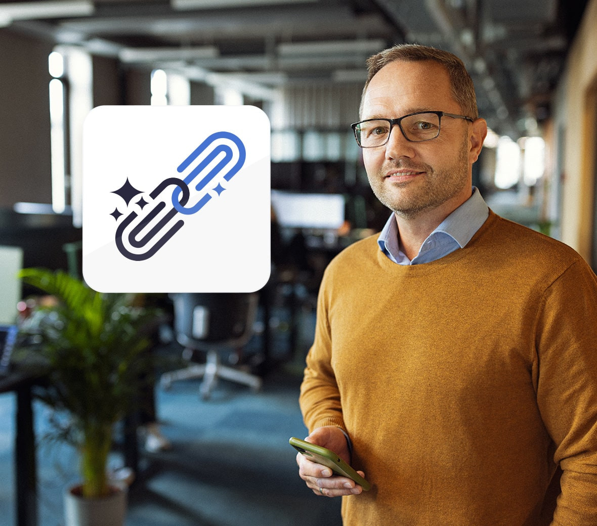 En mand står i en orange trøje med en smartphone i hånden og smiler ind i kameraet