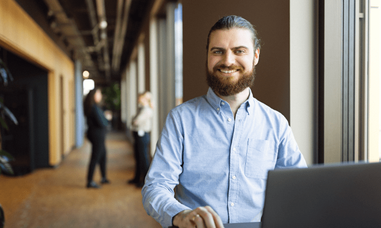 En mand sidder ved en computer på en gang og smiler ind i kameraet
