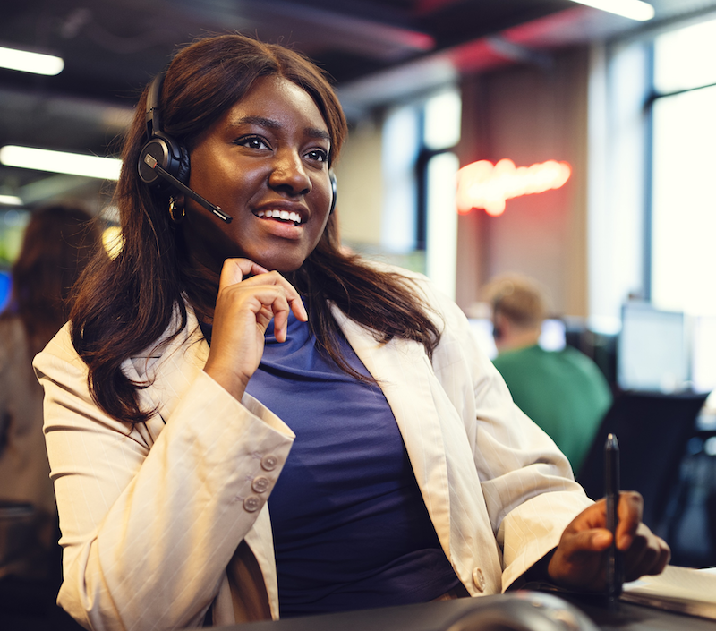En kvinde sidder og smiler med headset på