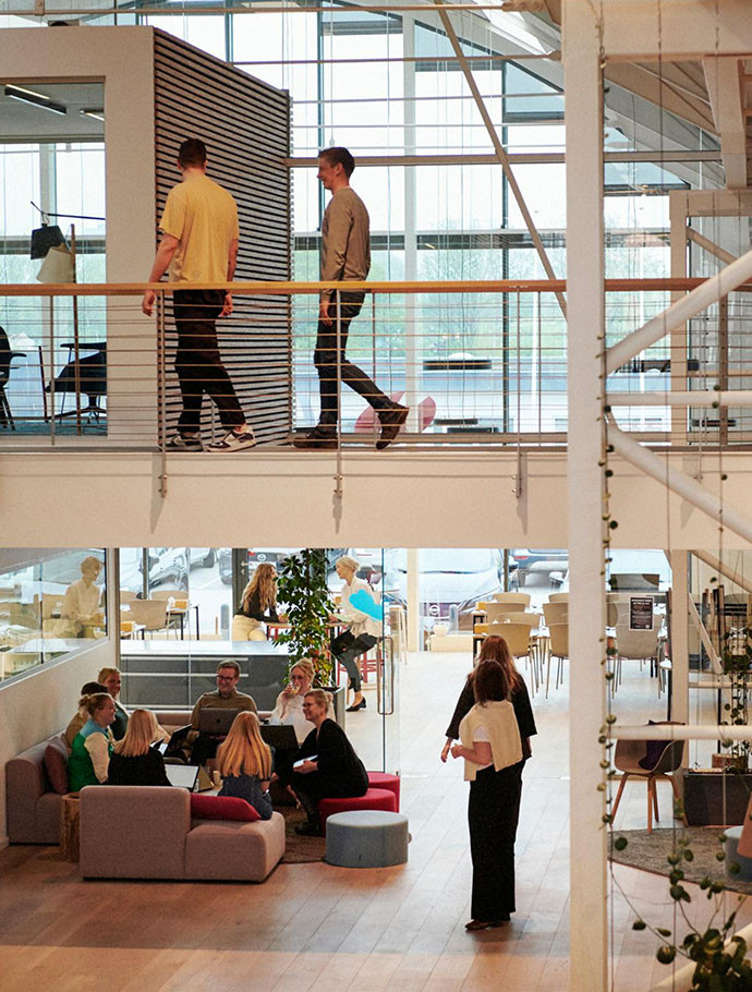 Et billede fra en virksomhed, hvor man kan se mennesker både sidde ved borde og gå oppe på en etage overnpå