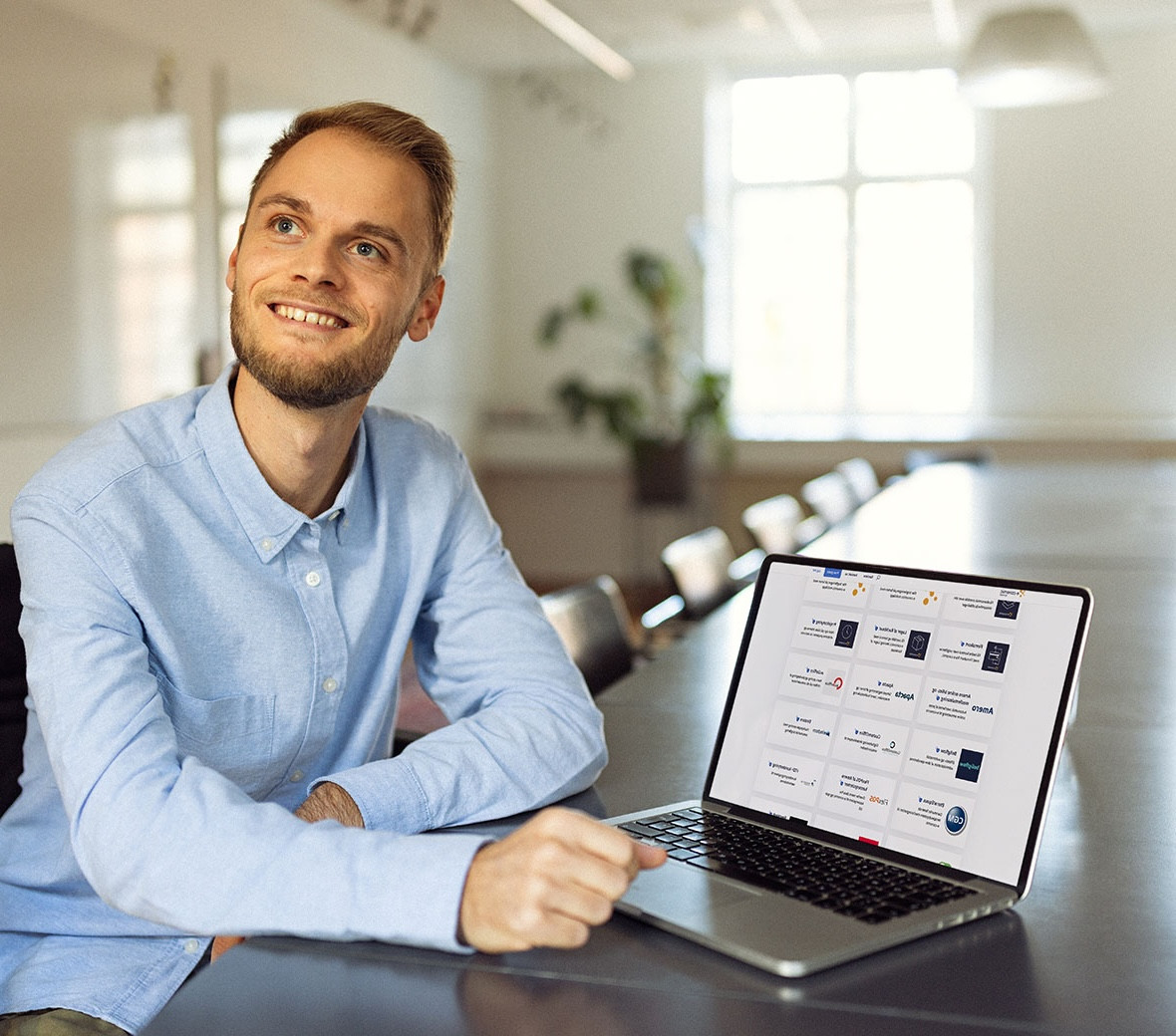 En mand sidder ved et bord med en computer og smiler op mod noget, man ikke kan se til højre for kameraet