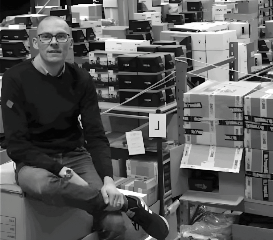 Et billede af en mand, der sidder på et lager blandt papkasser