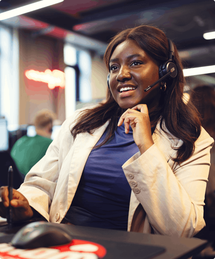 En kvinde med headset på sidder ved en computer og kigger smilende på skærmen