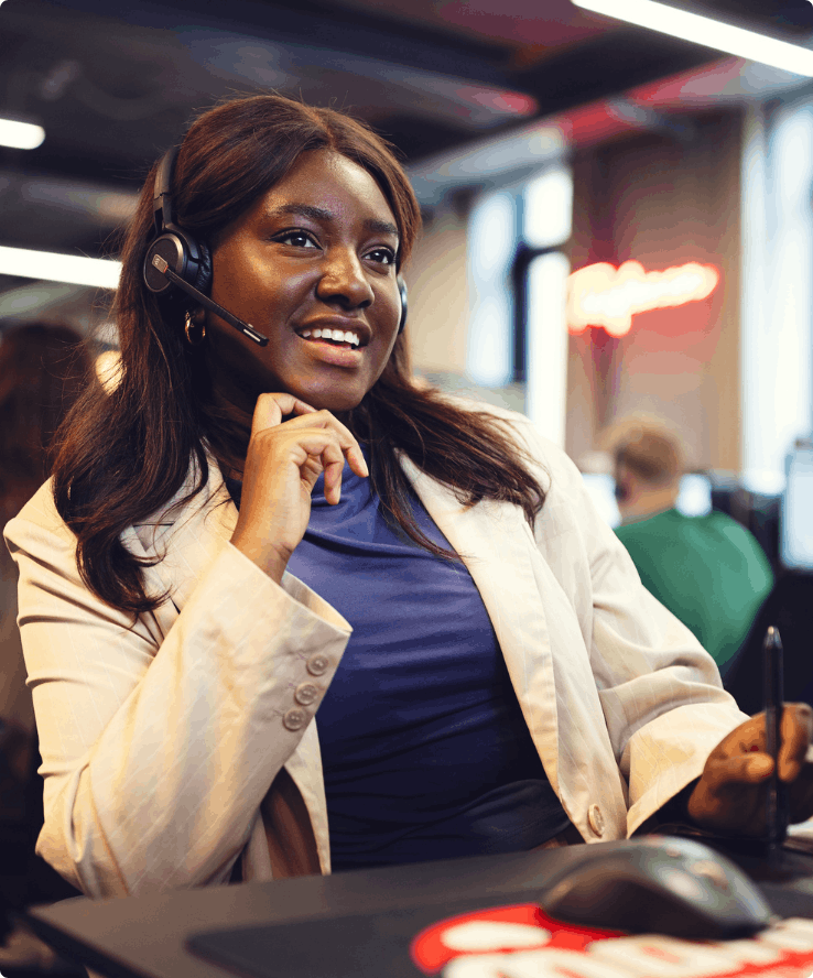En kvinde med headset på sidder ved en computer og kigger smilende på skærmen