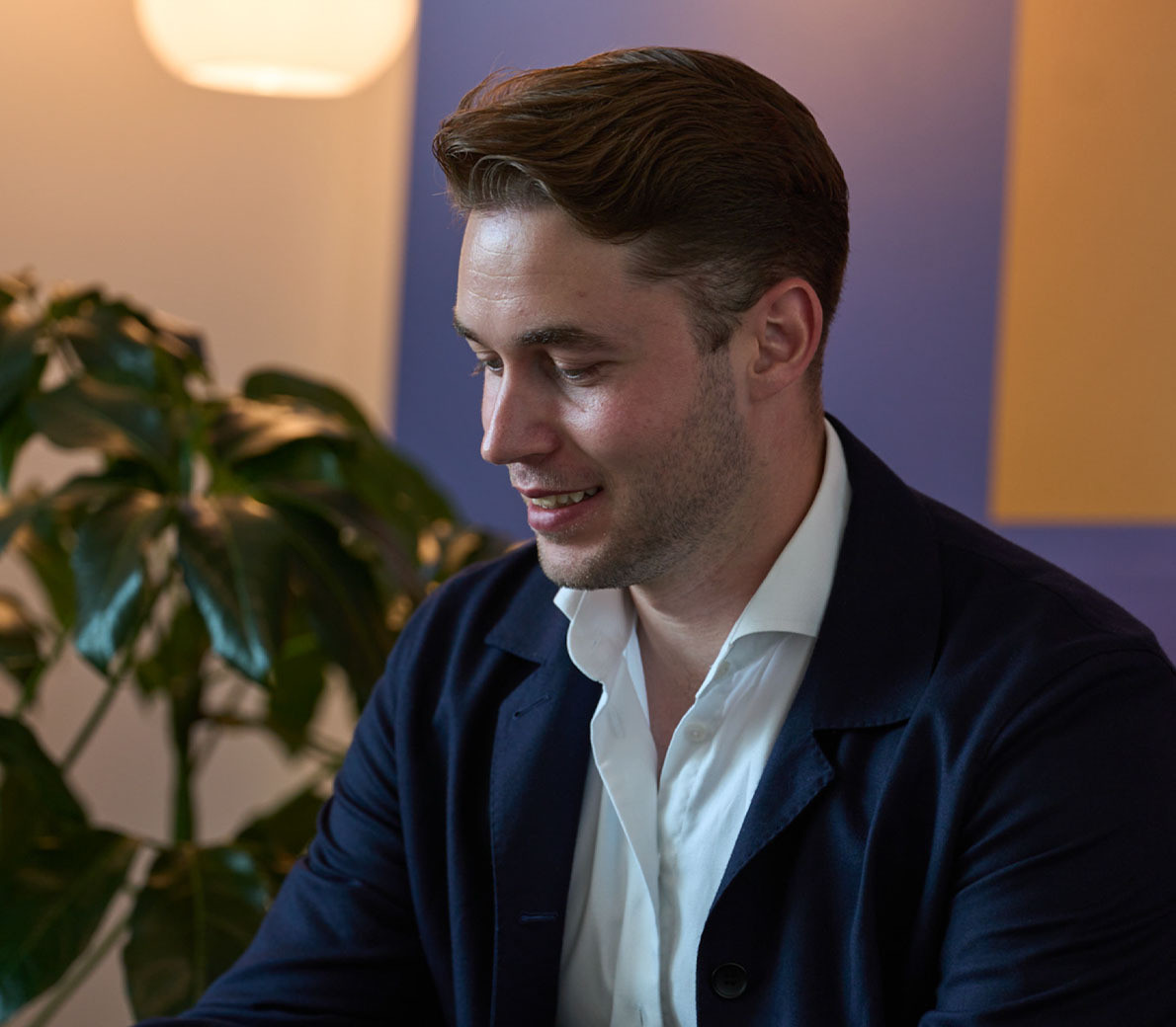 mand i hvid skjorte og blå jakke smiler