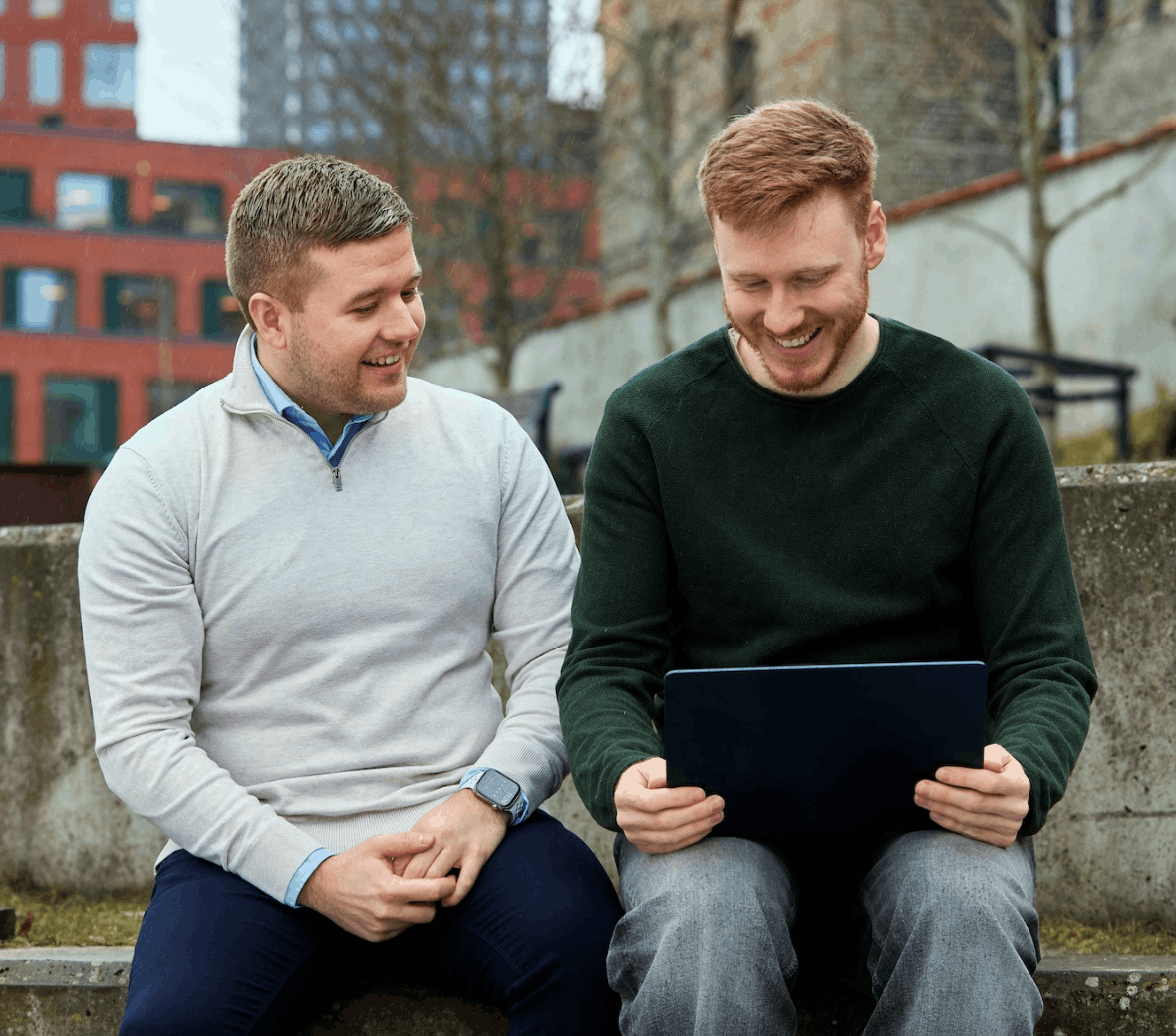To mennesker sidder udenfor og kigger på en tablet, som den ene holder i hånden
