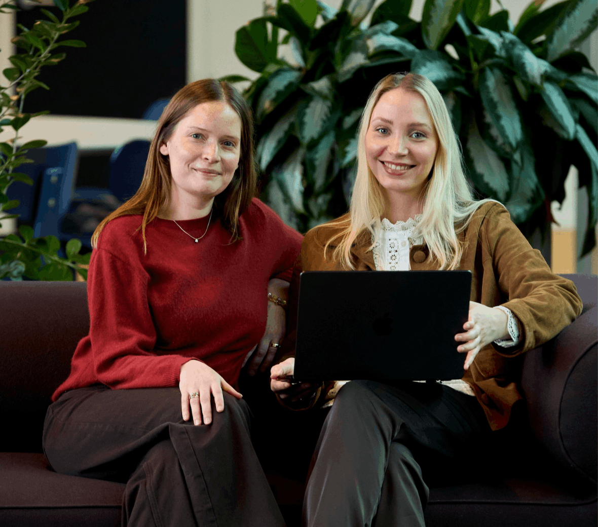 To personer sidder i en sofa med en laptop og smiler til kameraet