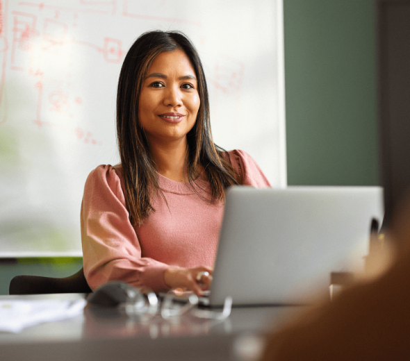 En kvinde sidder ved en computer og smiler til kameraet